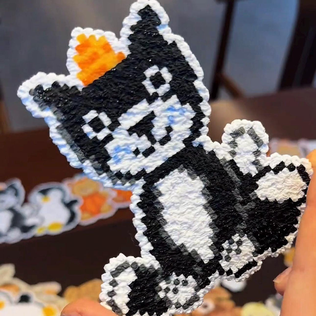 May include: A pixelated cat-shaped craft with a black and white body and an orange crown. The craft is made of textured plastic and has a retro video game aesthetic. Other similar crafts are visible in the background.