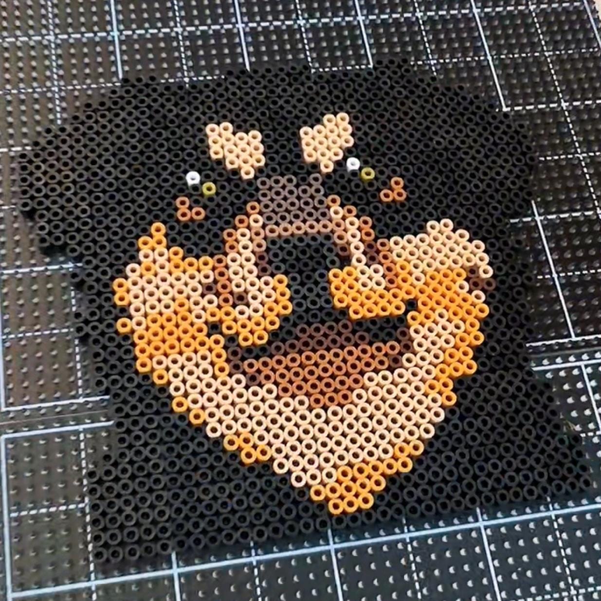 May include: A pixel art depiction of a Rottweiler dog's face, crafted from small black, tan, and brown beads. The dog's features are well-defined, with emphasis on the eyes and snout. The artwork is set against a grid background.