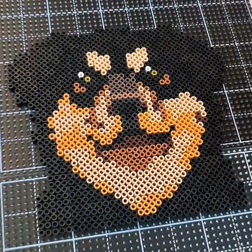 May include: A pixel art depiction of a Rottweiler dog's face, crafted from small black, tan, and brown beads. The dog's features are well-defined, with emphasis on the eyes and snout. The artwork is set against a grid background.