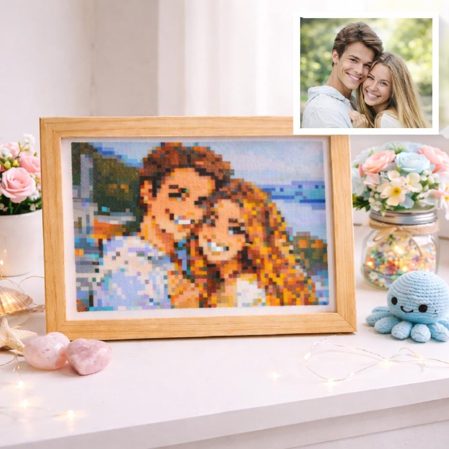 May include: A framed pixelated portrait of a smiling couple, in a wooden frame. A smaller photograph of the couple is in the upper right corner. The portrait is on a white surface, with flowers and a small blue crocheted octopus.